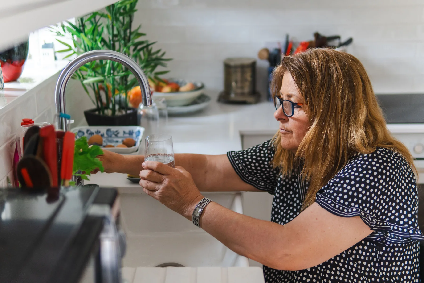 Person filling a glass with water in a home kitchen